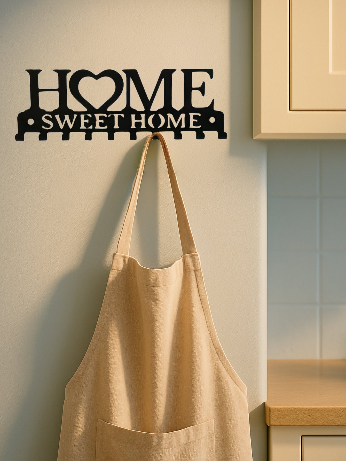 Beige apron hanging on a 'Home Sweet Home' wall decoration in a kitchen.
