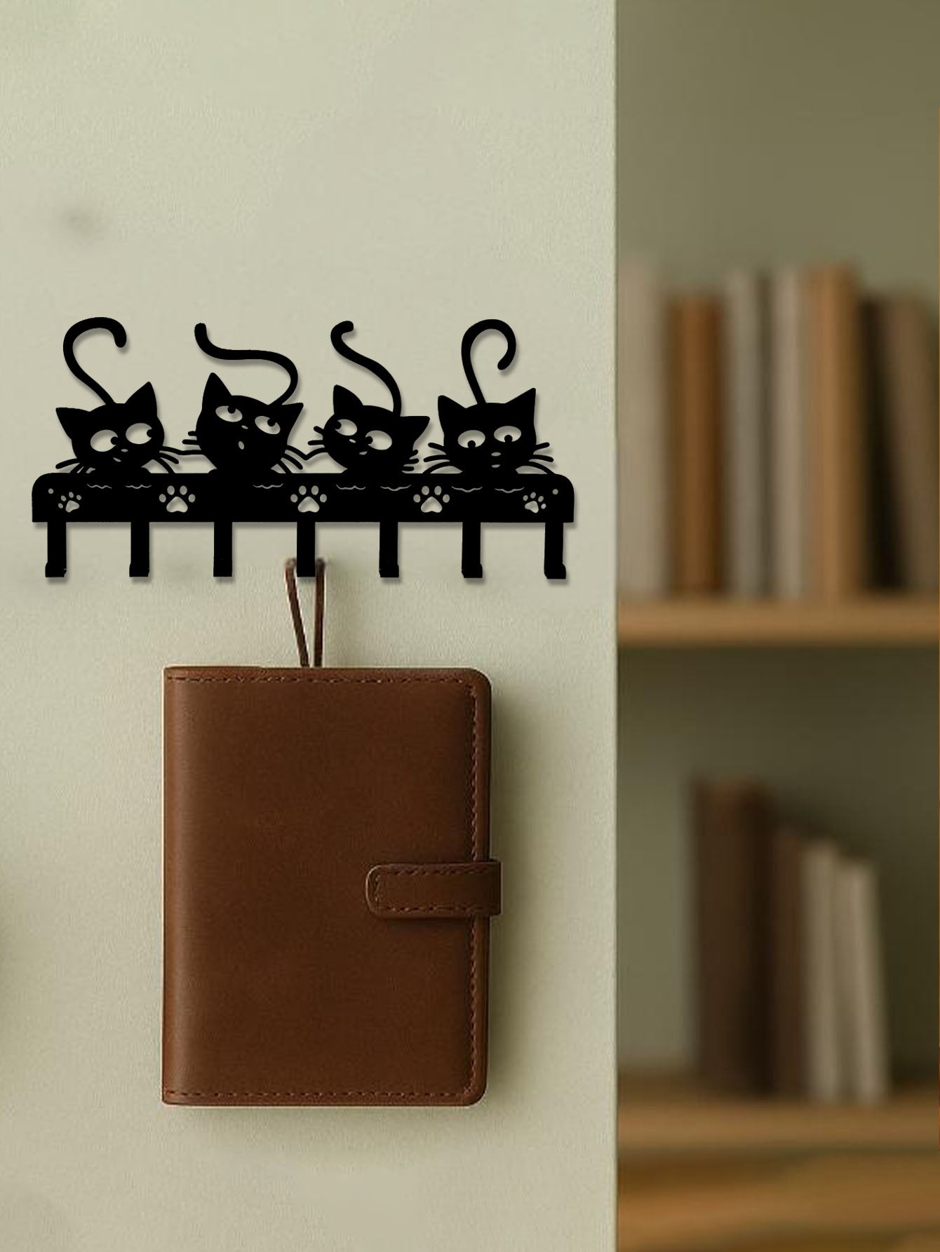 Black cat-shaped wall hook with a brown leather wallet on a white wall.