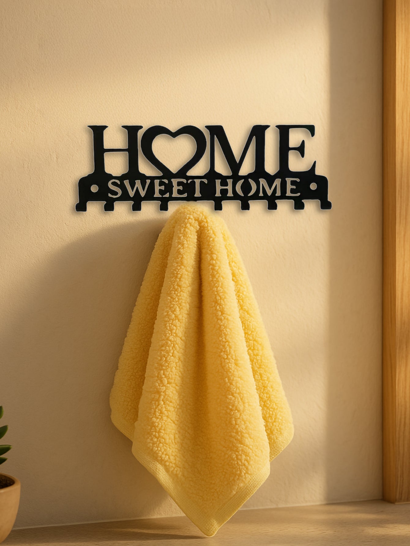 Decorative metal wall art with 'HOME SWEET HOME' text on a wall with a yellow towel hanging from it.