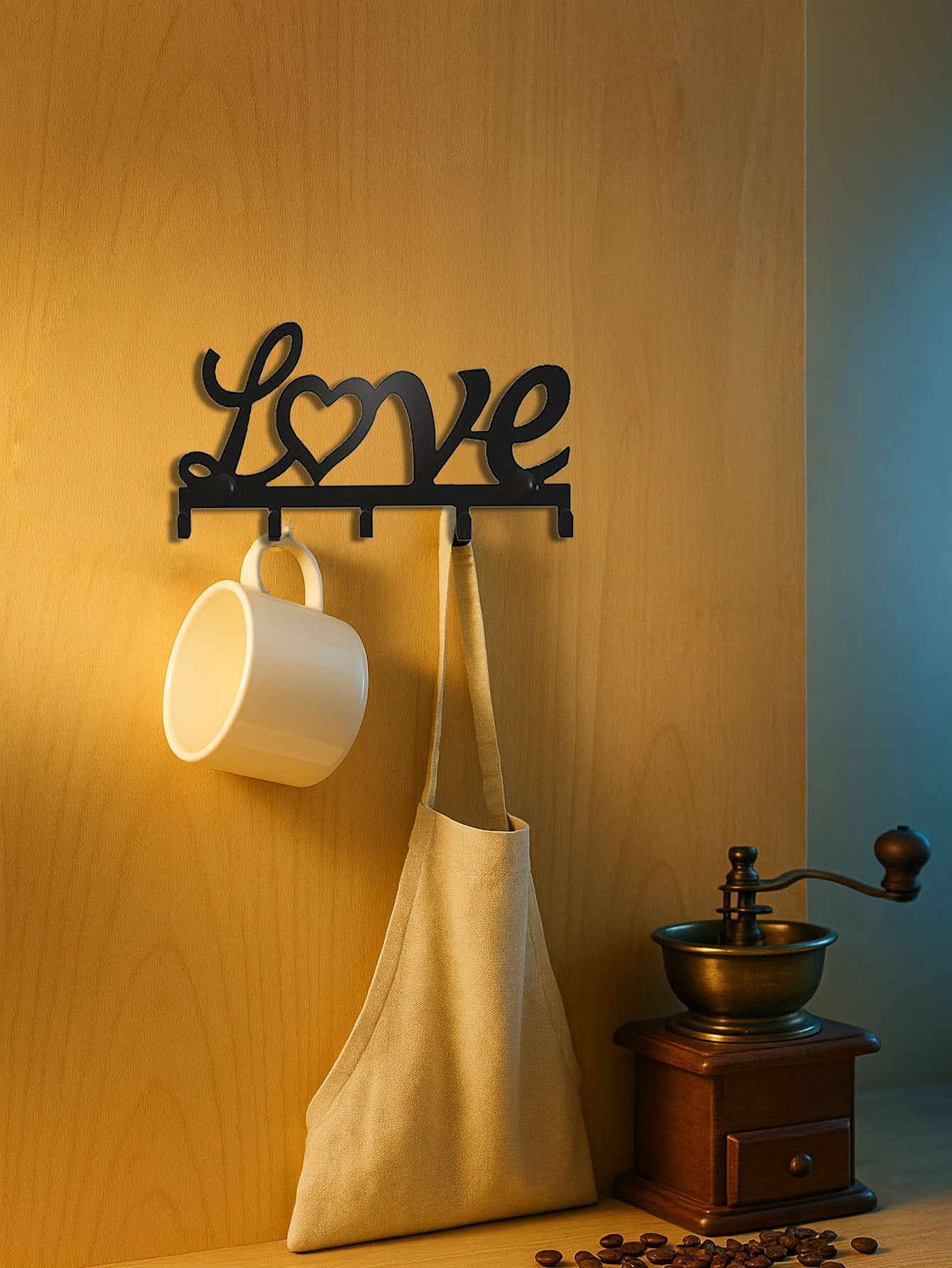 Decorative wall hook with 'Love' design, a white mug, beige bag, and coffee grinder on a wooden surface.