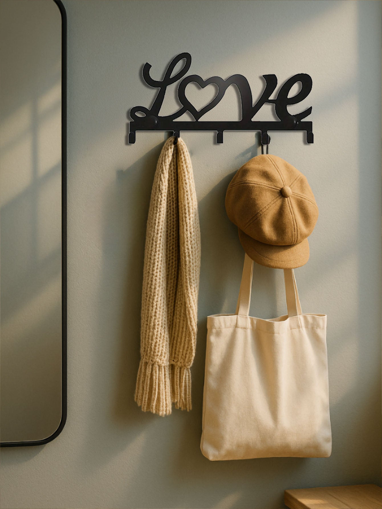 Decorative wall hook with 'Love' design, holding a scarf, cap, and tote bag against a neutral wall.
