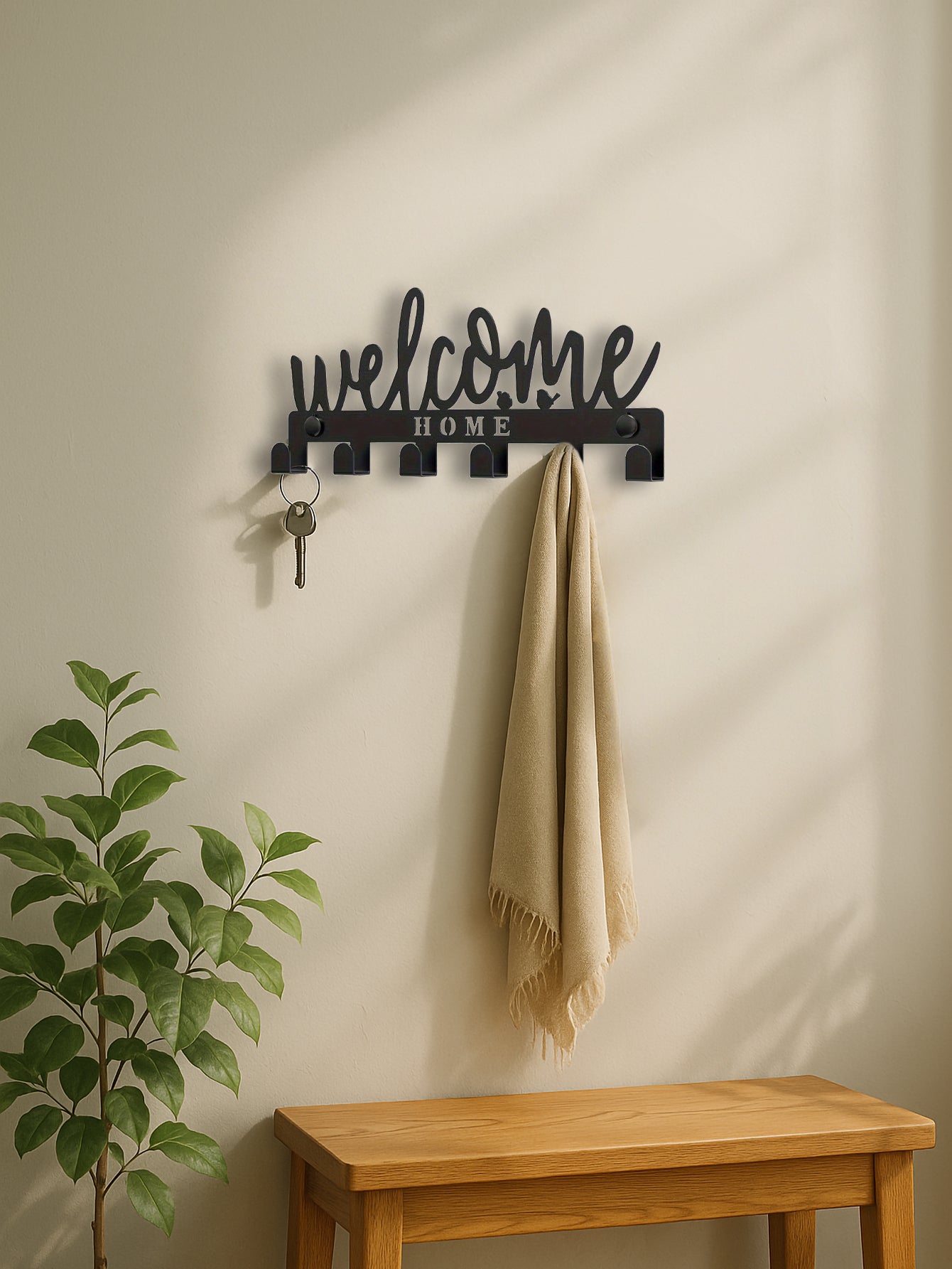 Decorative wall hook with 'welcome home' text on a wall with a plant and wooden bench.