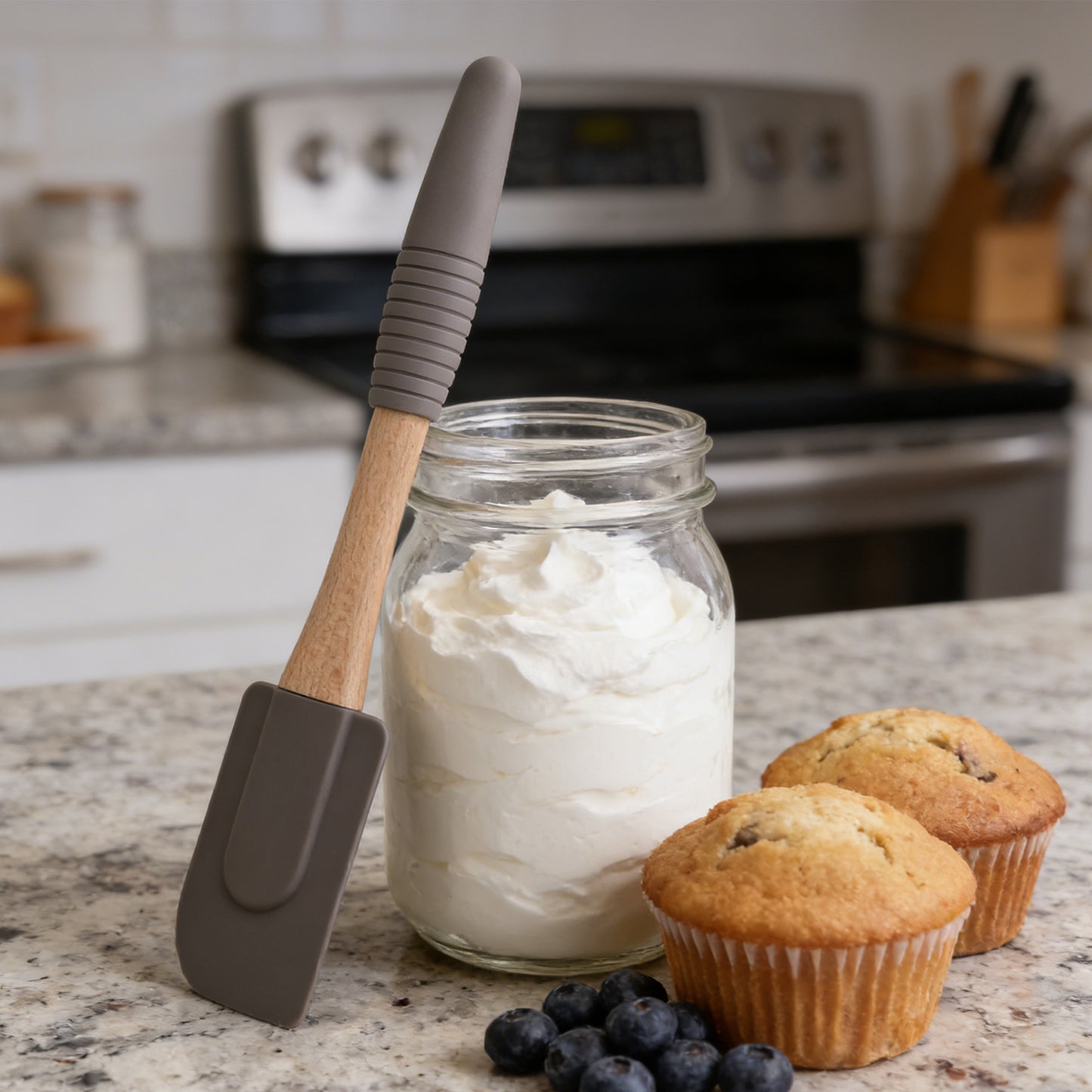 Jar of whipped cream with a spatula, muffins, and blueberries on a kitchen counter.