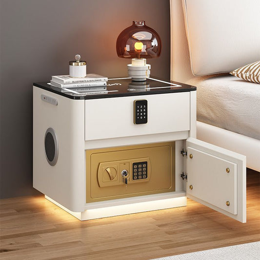 White nightstand with gold safe compartment and lamp on top in a bedroom setting.